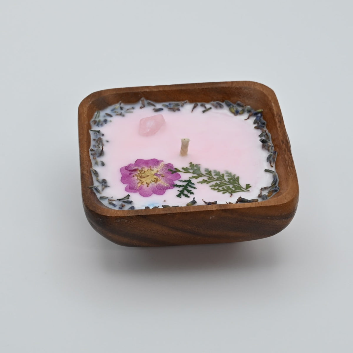 Right view of a 4-inch acacia wood bowl candle with pale wax and pressed purple flowers.
