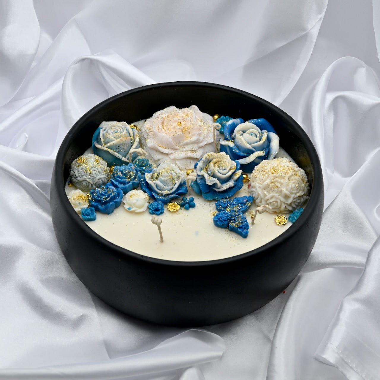 Close up view of black acacia wood bowl candle with blue and white floral wax design and gold accents