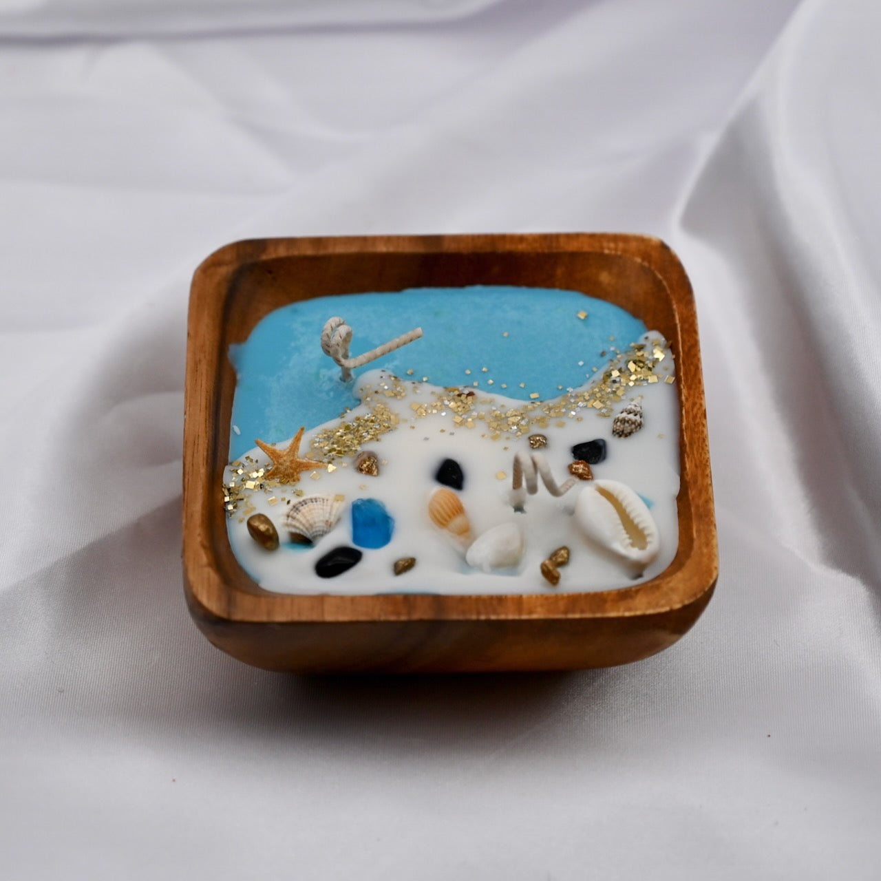 Close up of square acacia wood bowl candle with seashell and starfish wax details
