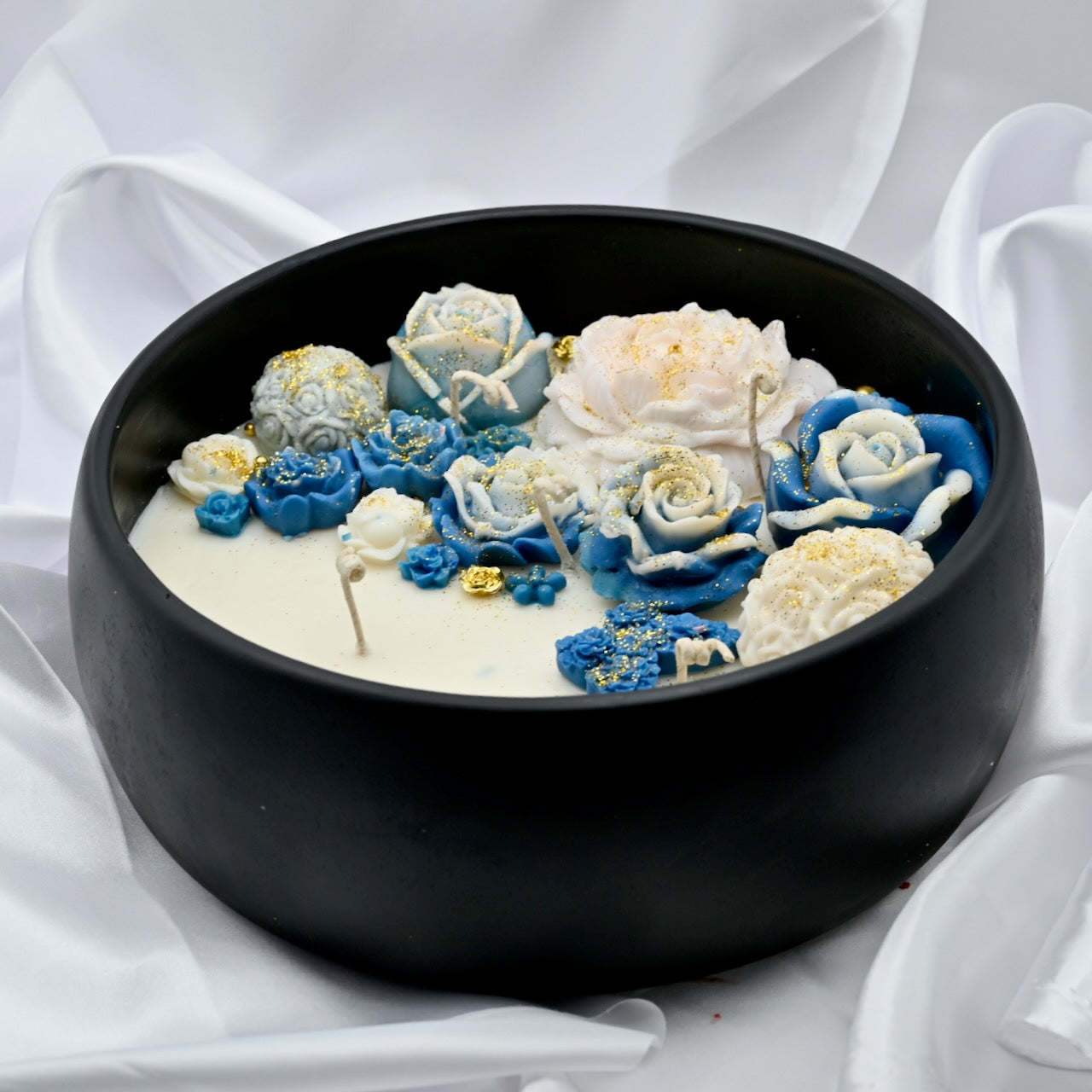 Close up of black acacia wood bowl candle with blue and white floral wax design and gold accents