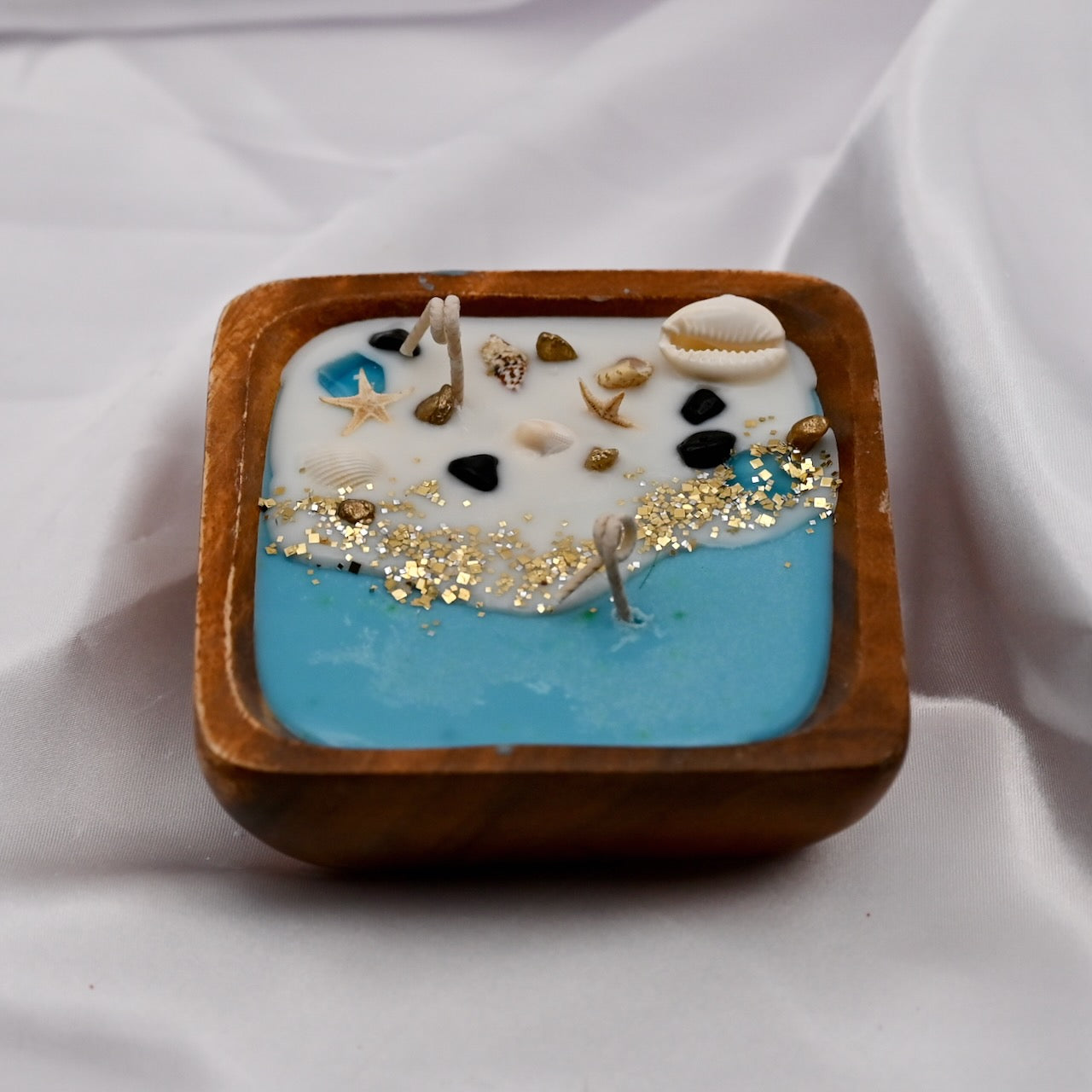 Detailed view of square acacia wood bowl candle with seashell and starfish wax details