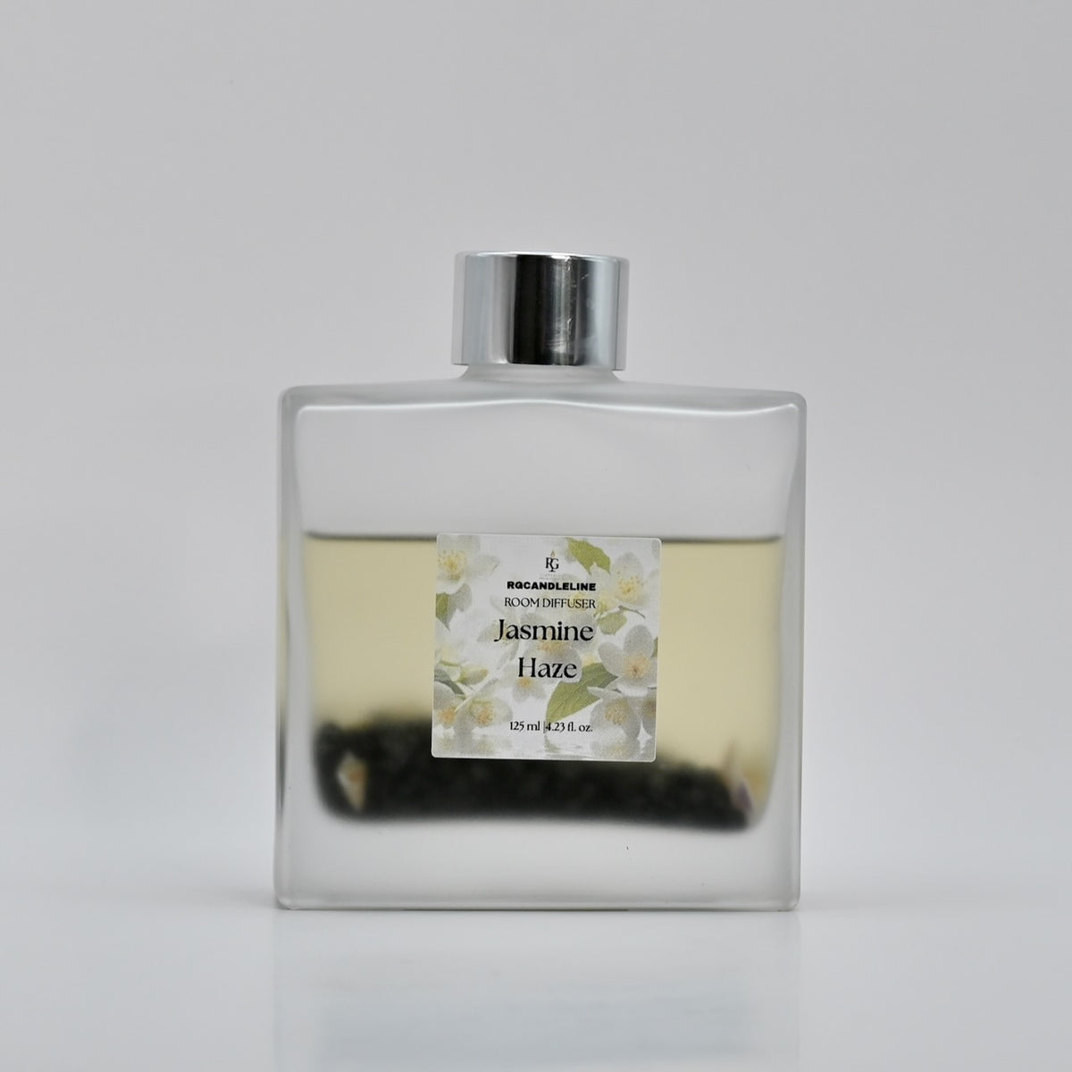 Jasmine Haze frosted square room fragrance diffuser with a silver cap, floral label, and dark decorative accents.
