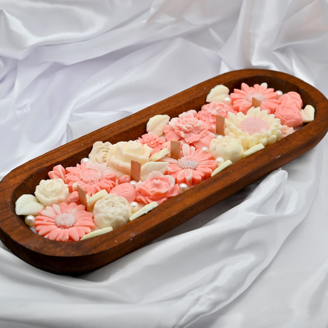 Wooden tray with pink and white floral-shaped candies on a white fabric background
