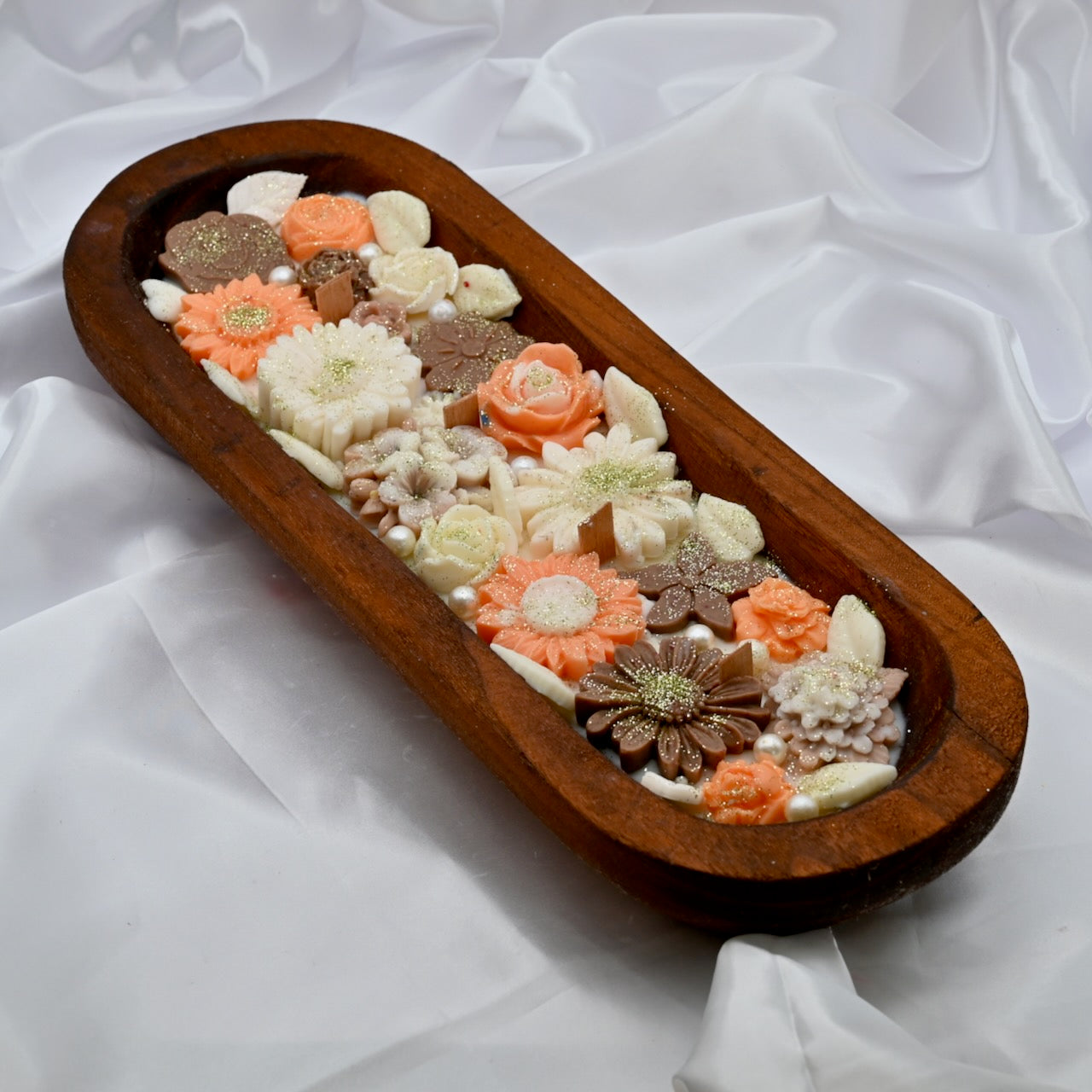 Left close up view of wooden tray with multiple floral-shaped colorful pink and brown candles