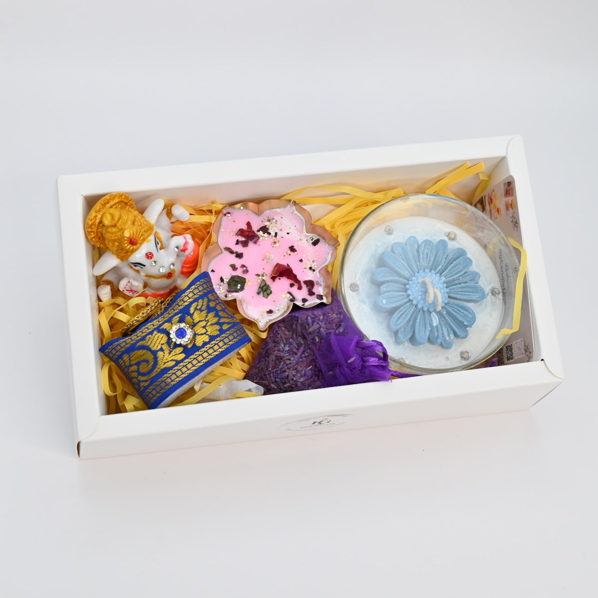 Open large white gift box showing two candles, Ganapati accent, decorative flower, and small bag