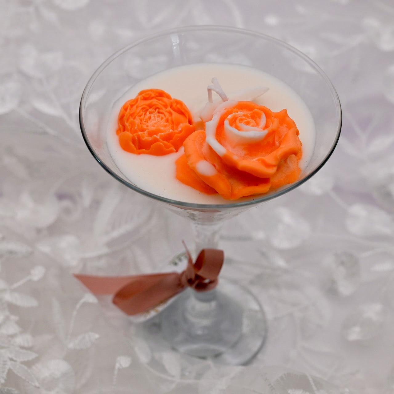 Glass container floral soy candle with orange rose-shaped wax flowers on a neutral background