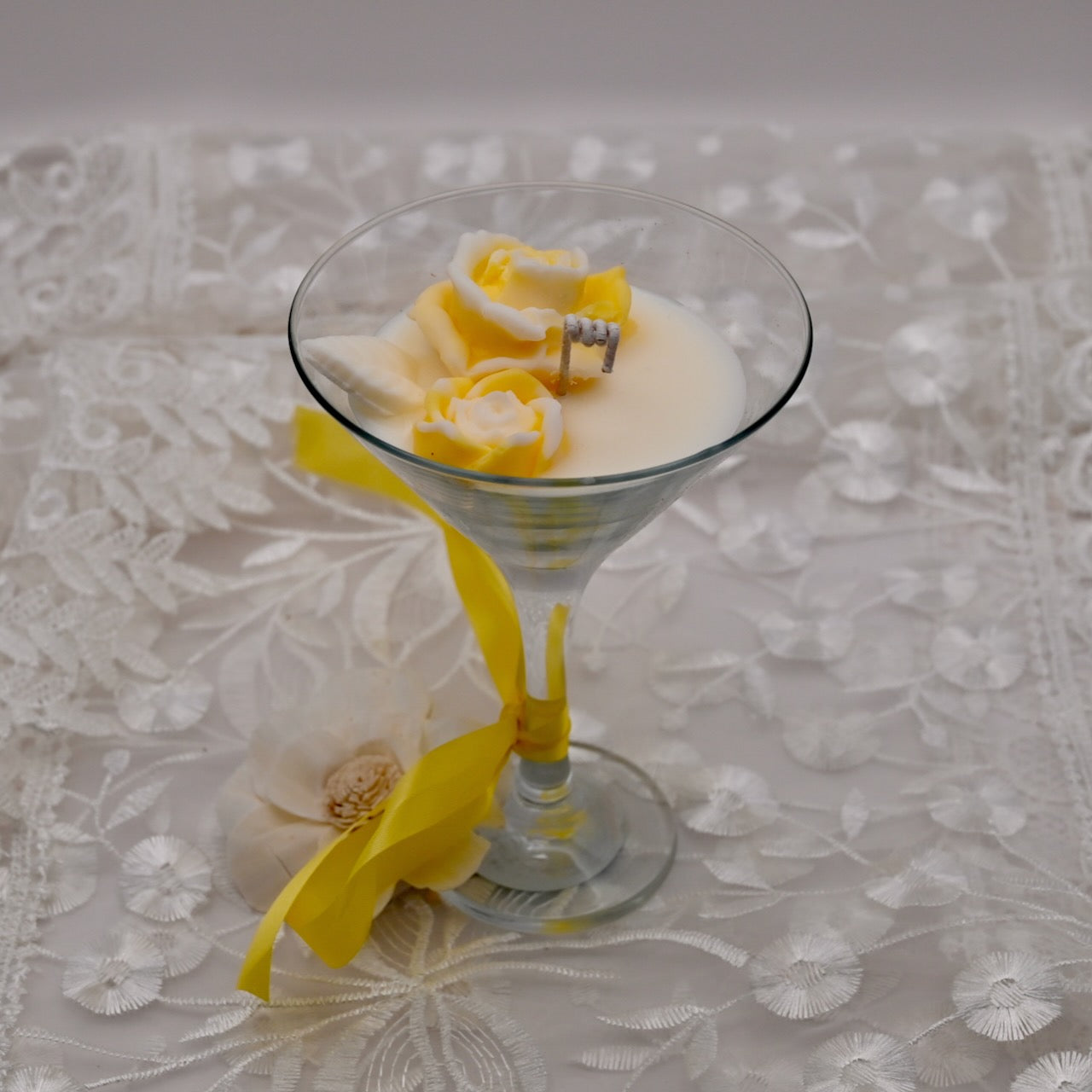 Glass container floral soy candle with yellow rose-shaped wax flowers on a neutral background