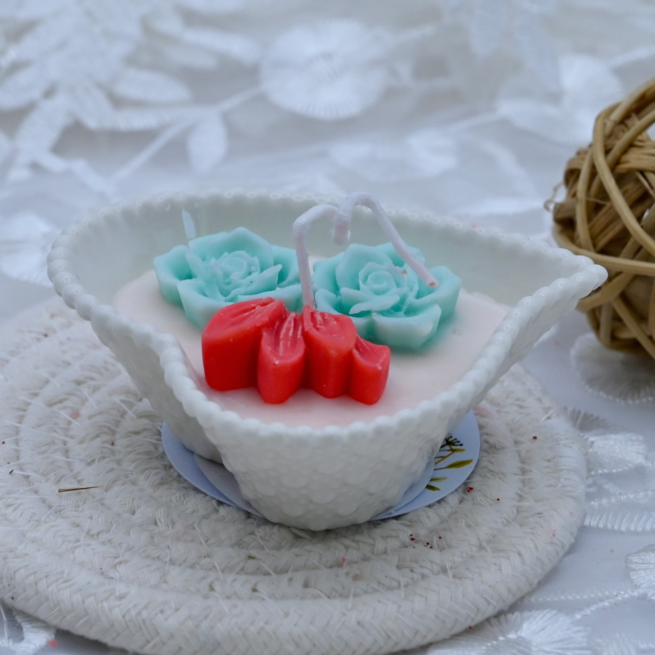 Decorative candle with cyan color flowers, and red accents in a white ceramic heart shaped container.