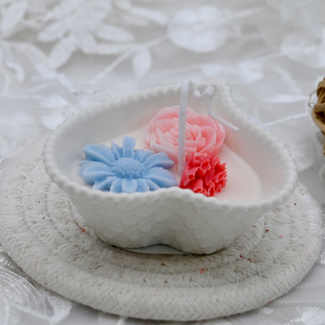 Decorative candle with blue daisy, ping rose, and red accents in a white ceramic heart shaped container.