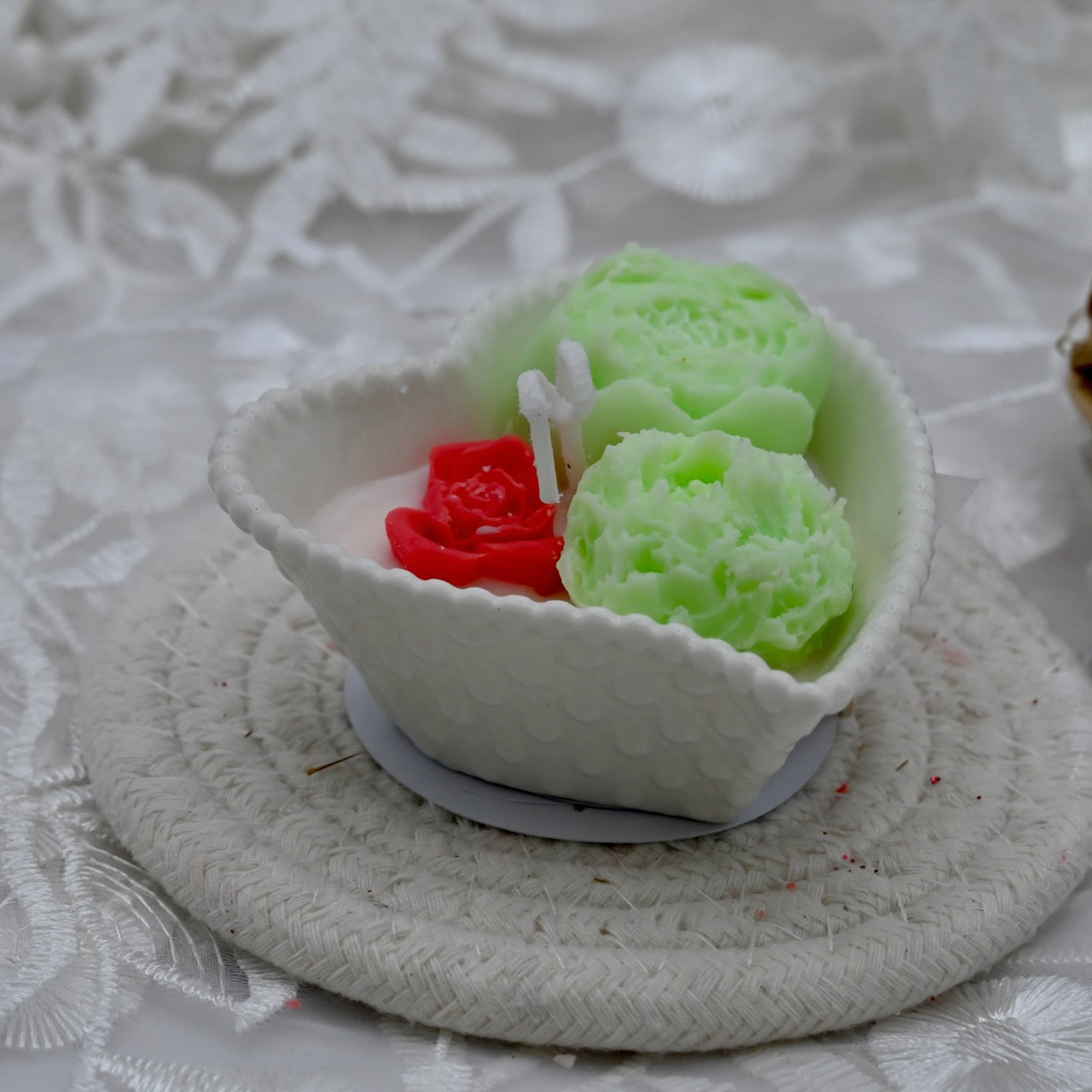 Decorative candle with green flower and red accent in a white ceramic heart shaped container.