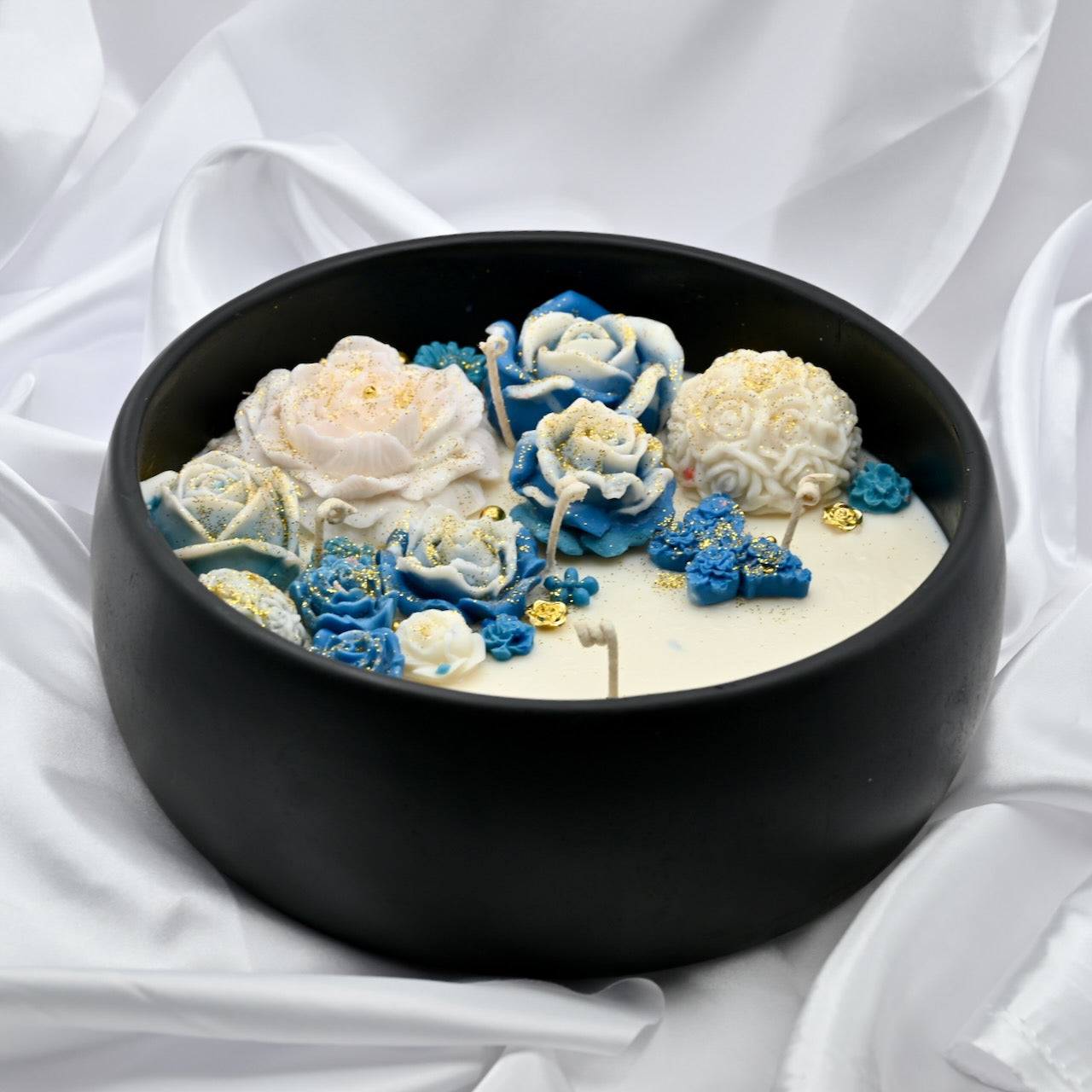 Left view of black acacia wood bowl candle with blue and white floral wax design and gold accents