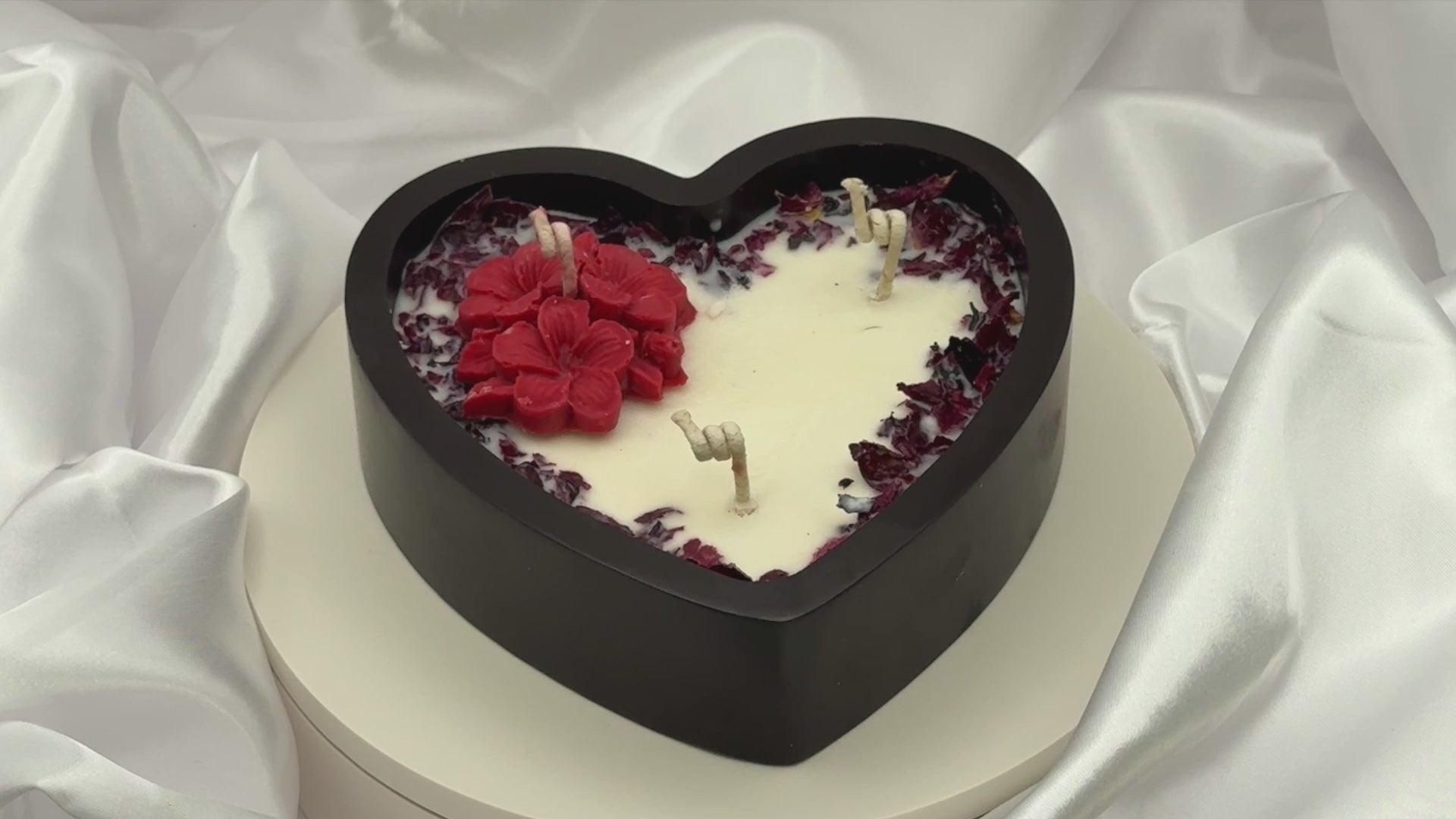 Video of heart-shaped candle with red and white design on a white fabric background