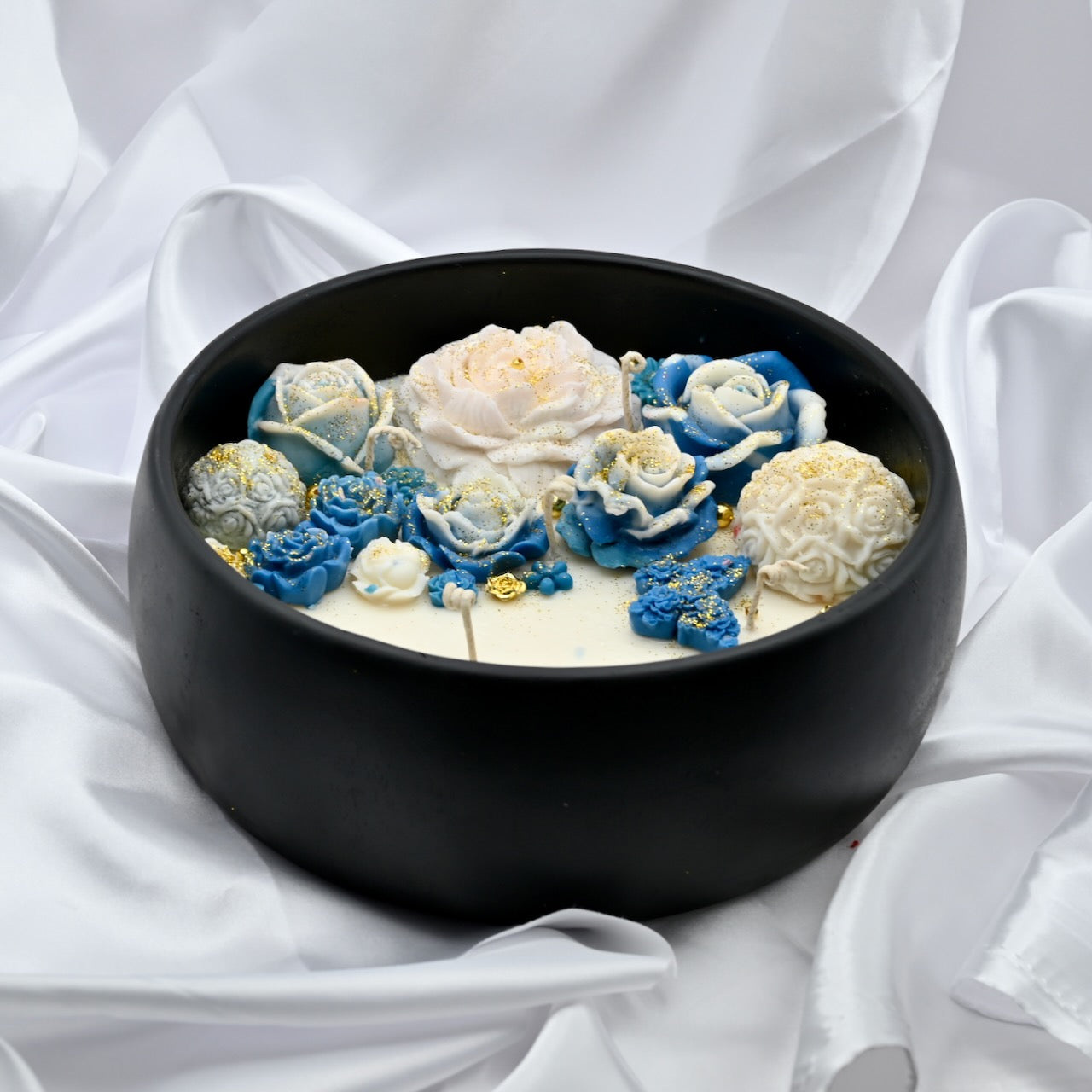 Side close up view of black acacia wood bowl candle with blue and white floral wax design and gold accents