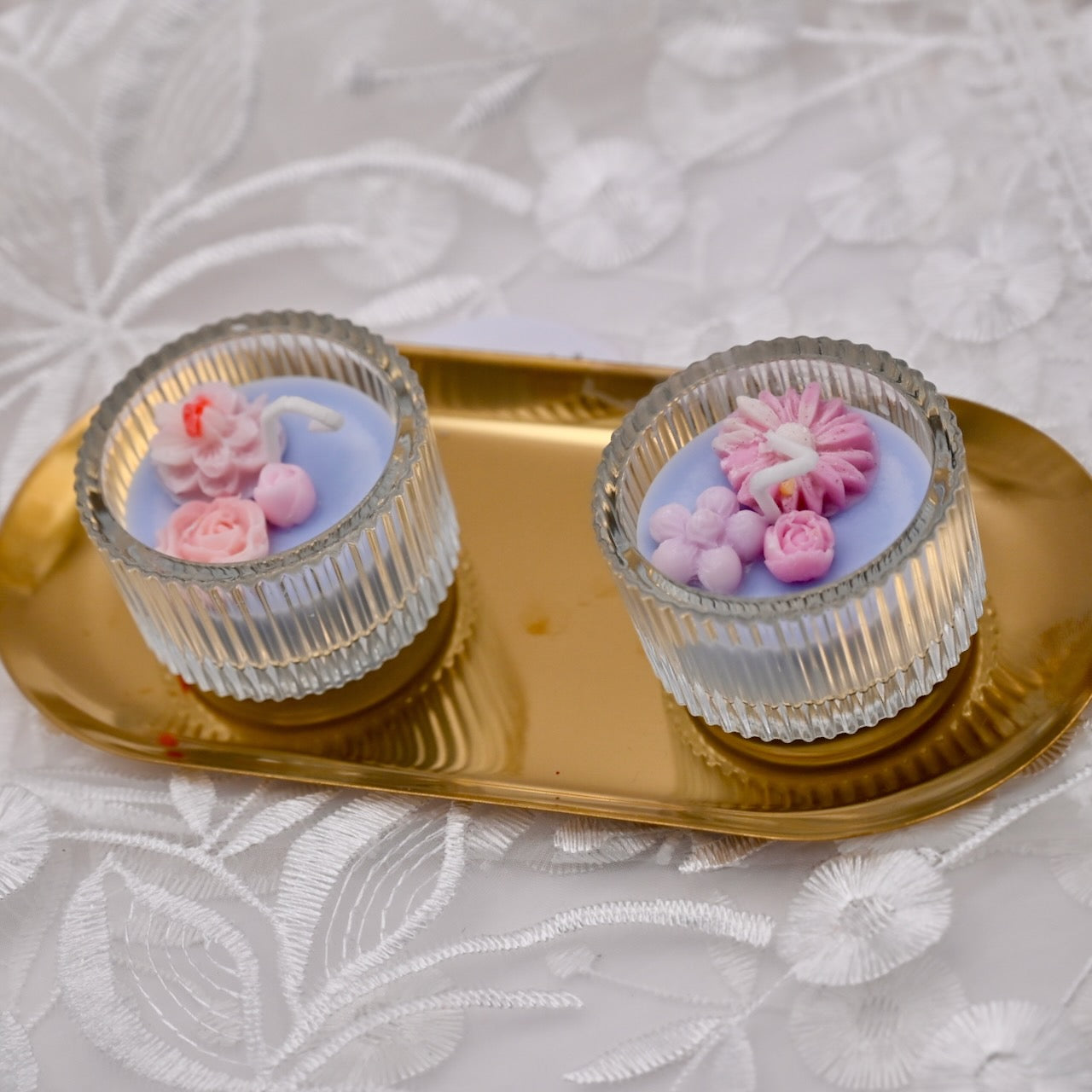 Two sky blue mini glass candles with decorative pink flowers on the top