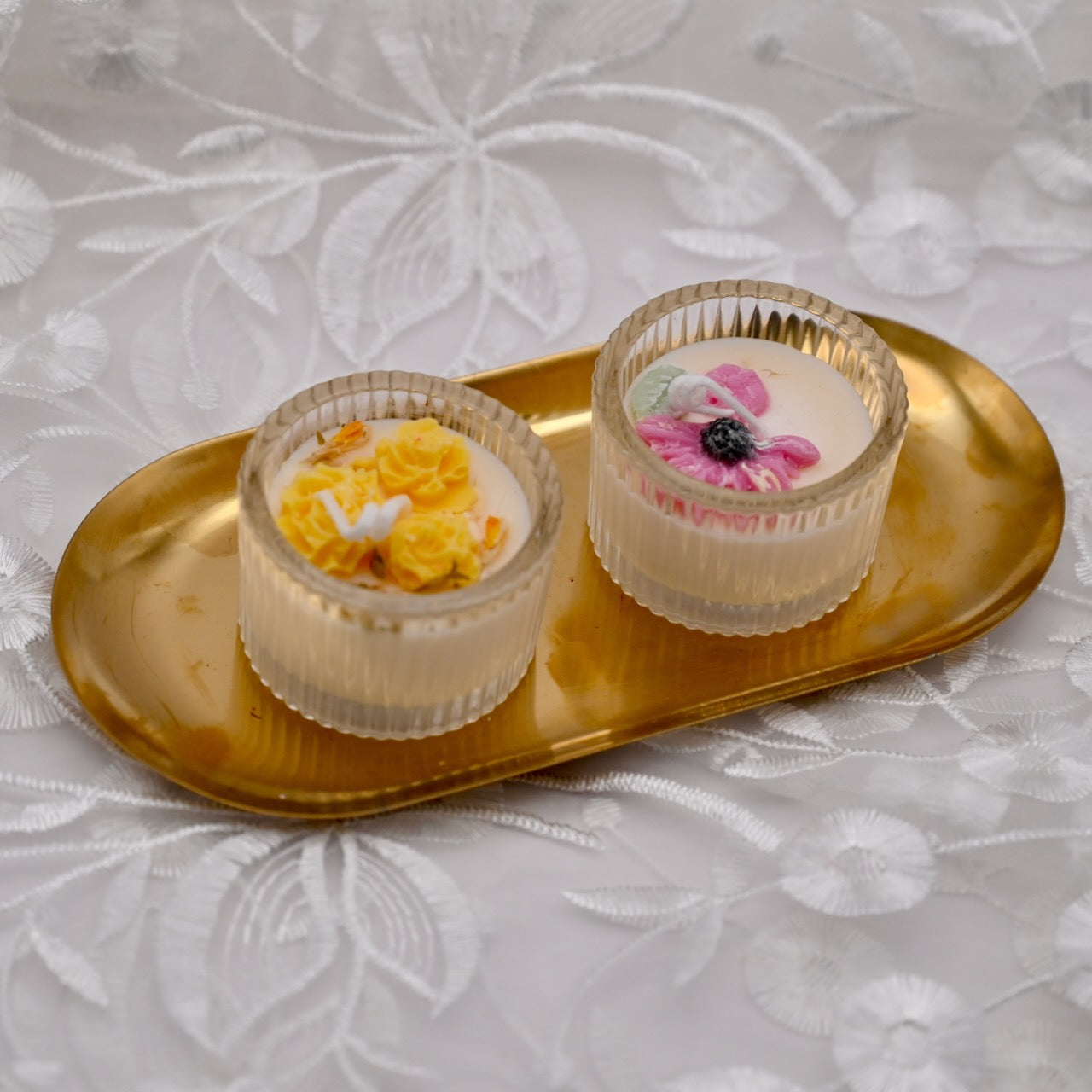 Two white mini glass candles with decorative flowers on the top